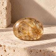 Sensorium Rutilated Quartz — Illumination, polished rutilated quartz on warm travertine