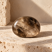 Sensorium Smoky Quartz — Ground, polished smoky quartz on warm travertine